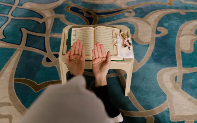 Voyageur musulman assis sur un tapis, mains levées en invocation, dans un paysage désertique.